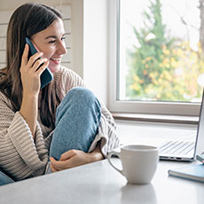 1 una mujer joven esta sentada en la cocina con un telefono inteligente y una computadora portatil